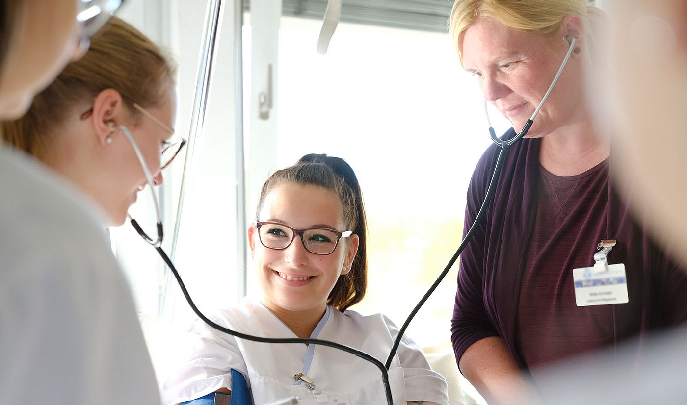 Lehrerin erklärt ihren Schülerinnen in der Pflegeausbildung wie man den Blutdruck misst