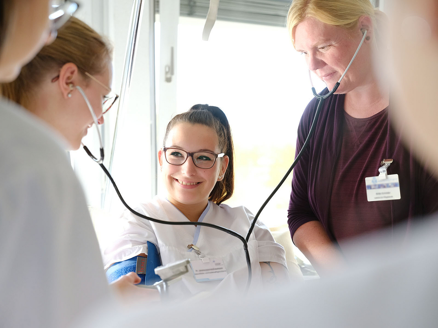 Lehrerin erklärt ihren Schülerinnen in der Pflegeausbildung wie man den Blutdruck misst