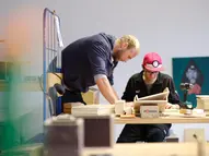 Fachanleiter beugt sich zu einem Teilnehmer, der etwas aus Holz baut